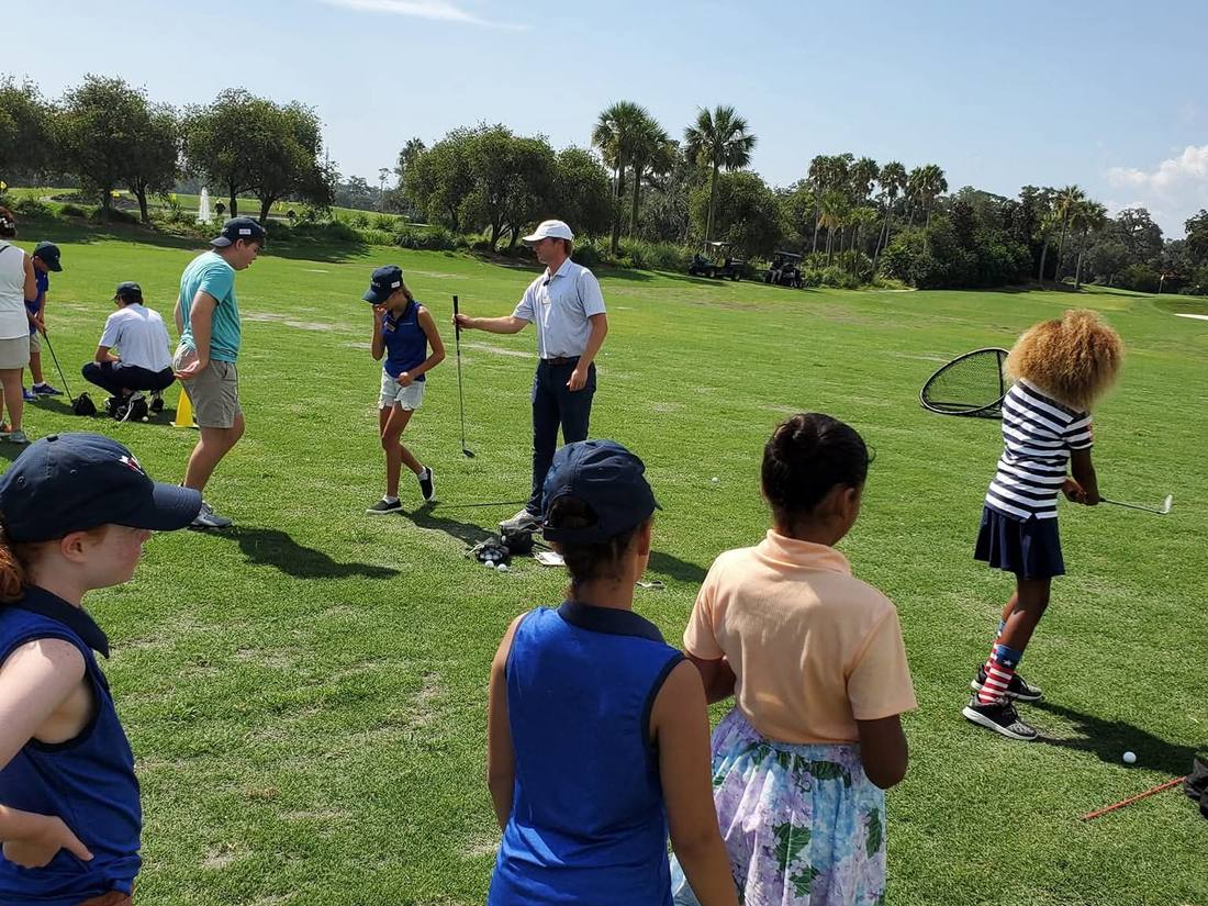 A PGA coach leads young golfers through a lesson on the range at TPC Sawgrass