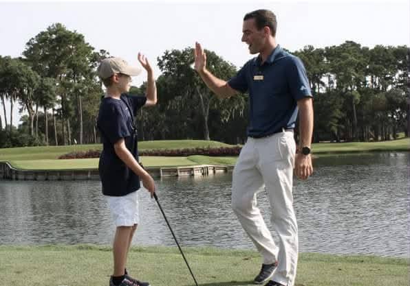 A young golfer and a coach high-five beside the water at TPC Sawgrass